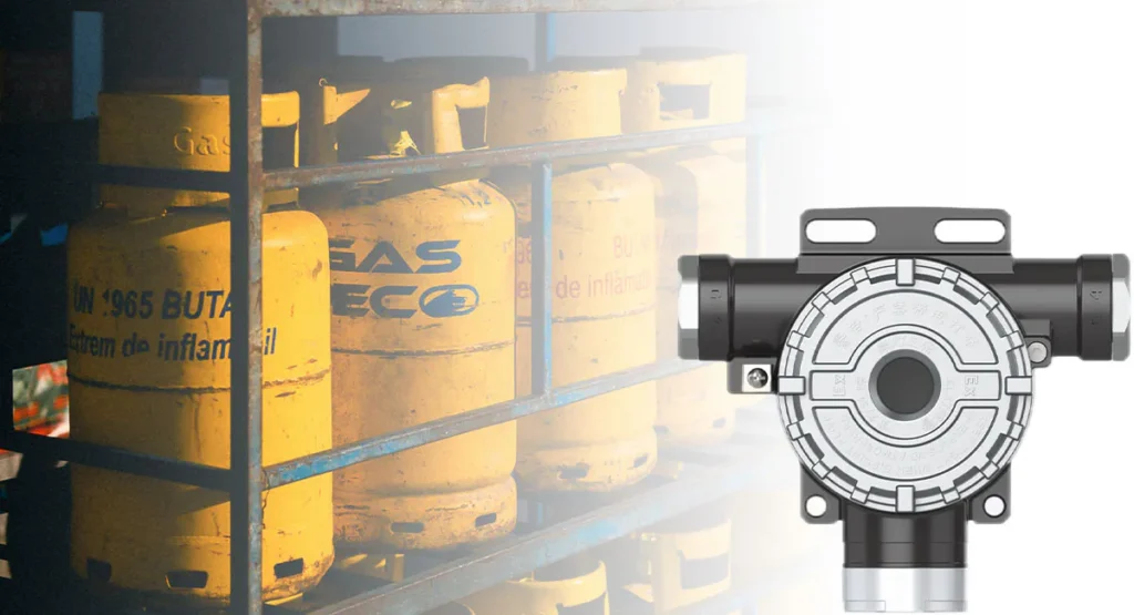 Détecteur de gaz naturel et de monoxyde de carbone représenté avec un stockage de bouteilles de gaz industriel à l'arrière-plan, utilisé pour la surveillance des fuites de gaz combustibles et toxiques