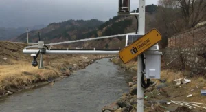 Water level sensor and monitoring equipment installed along a river, equipped with a camera and solar panel, used for real-time water level monitoring and environmental data collection.