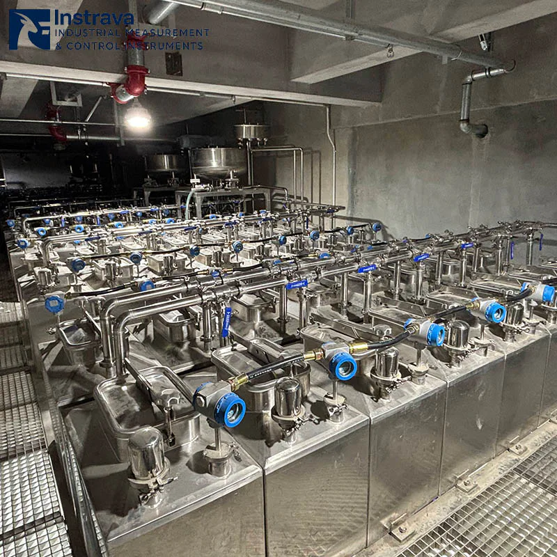 Real-world scene of an industrial tank farm level monitoring system, showing rows of professional industrial instruments installed on stainless steel vessels.